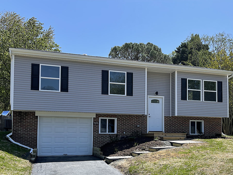 After: the same raised ranch with new gray siding, black shutters, a new garage door and a paved drive